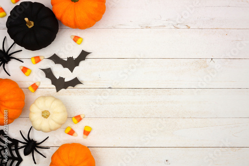 Halloween side border with black, orange and white decor and candy over a white wood background. Top view with copy space.