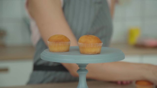The female confectioner puts the muffin (cake) on the confectionery stand to record a culinary blog with the decorating process. Decoration of confectionery: preparation of a capcake.