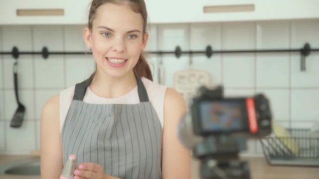 A modern woman shoots a video of the process of making dessert - a capcake confectionery vlog. Opposite the confectioner is a tripod with a camera, she writes a video blog. Culinary master class.