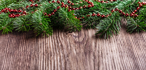 Fototapeta na wymiar Fir tree branches with Christmas red garland beads decoration on wooden rustic background.