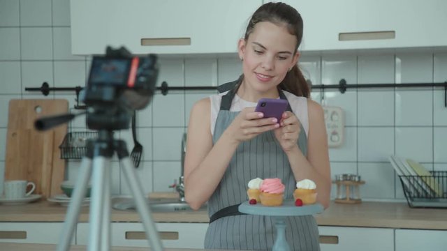 Confectionery blog. Housewife cooked cakes, put them on a stand and photographed them to make a post in blog. Pastry vlog. Confectioner decorates the capcake and then takes pictures on the smartphone