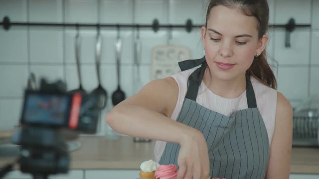 Confectionery blog. Housewife cooked cakes, put them on a stand and photographed them to make a post in blog. Pastry vlog. Confectioner decorates the capcake and then takes pictures on the smartphone