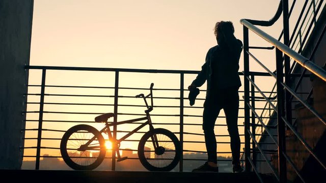 Young man is jumping from the railings and going away with his bike during sunset