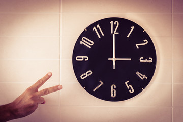 Big black clock on white wall. Time change. DST. Survey of the European Union on time change. Gesture of victory. Caucasian man.