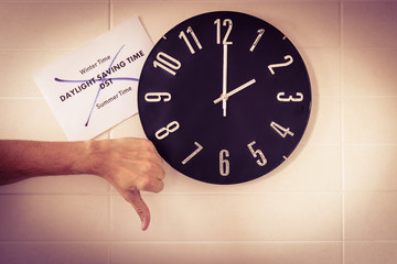 Big black clock on white wall. Time change. DST. Survey of the European Union on time change. Gesture of disagreement . Thumb down of Caucasian man. Banner with text. English.