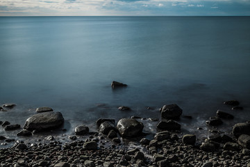 Obraz premium Standing at the shore where the ocean meets the land. It's the baltic sea in winter. A quiet, smooth evening in the middle of blue and grey light an colour.