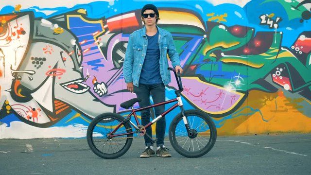 Teenager is standing with his BMX beside a painted street wall