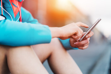 Woman resting after sport on the street and using cell phone, close-up