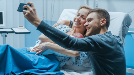 Father Takes Selfie of Him with His Wife Holding Newborn Baby while Lying on the Hospital Bed....