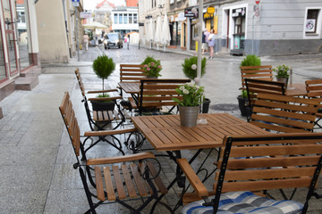 A metal bench with a round table and an empty chair in front of a cafe on the street