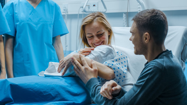 In the Hospital Mother Hold Newborn Baby, Supportive Father Lovingly Hugging Baby and Wife. Happy Family in the Modern Delivery Ward.