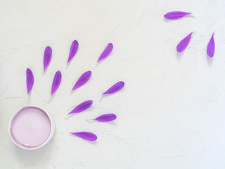 Purple cosmetic cream and purple flower petals on white background. Creative beauty fashion cosmetics photo. Flat lay