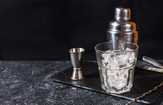 Bar tools for making cocktail. Shaker and a glass of ice on dark stone table.