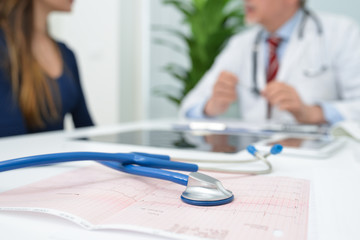 Stethoscope on an electrocardiogram, doctor and patient in the background