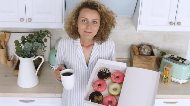 Young Woman Wearing Pajamas Having Breakfast With Coffee And Doughnut On Kitchen