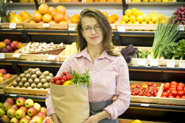 Happy woman holding a paper bag with food, vegetables and fruits. 