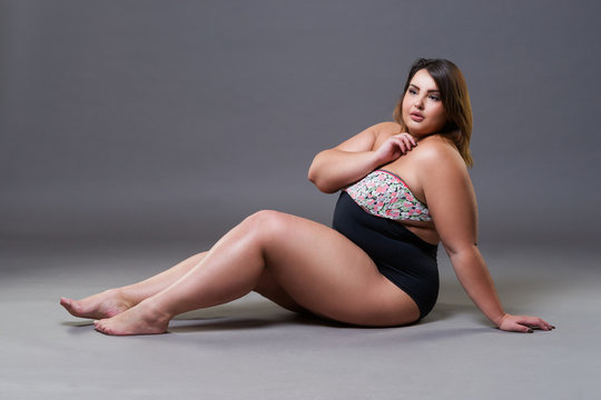 Plus size model in sexy swimsuit, fat woman on gray background, overweight female body