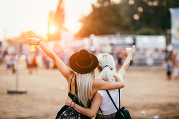 Two female friends drinking beer and having fun at music festival.Back view
