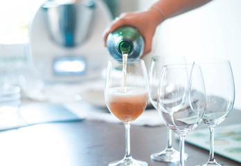 human hand isolated serving cidre champagne beer from a green glass bottle in wine glasses with kitchen in background