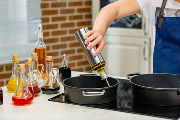 Woman pouring cooking oil from bottle into frying pan on stove