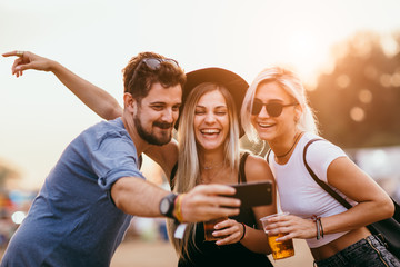 Group of friends drinking beer and taking selfie at music festival 