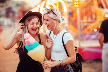 Foto auf Acrylglas Vergnügungspark Aufnahme von glücklichen Freundinnen im Vergnügungspark, die Zuckerwatte essen. Zwei junge Frauen genießen einen Tag im Vergnügungspark.