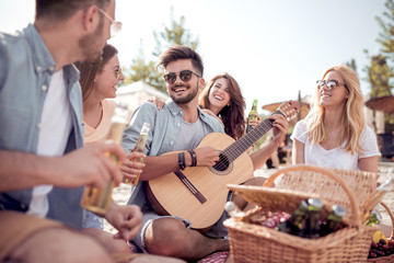 Group of friends with guitar having picnic on the beach