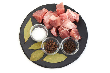 Raw pork meat with spices on a shale slate plate, isolated on white background.