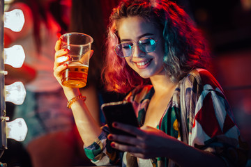 Young woman at the festival drinking beer and using mobile phone 