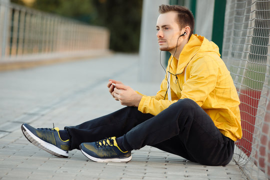Runner man athlete sitting at outdoor stadium listening to music with his earphones. Respite.