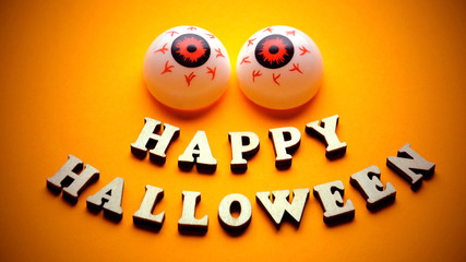 HAPPY HALLOWEEN. Template for design for the holiday of all saints. A cheerful face with emotion from wooden letters and two balls of eye on a bright yellow background. Vignetting.