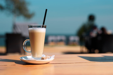 Glass Cup with hot latte and straws on a wooden table on the summer terrace of the cafe