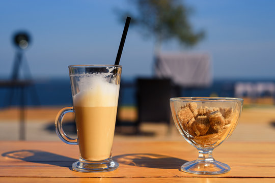 Glass mug with latte and salt shaker and sugar bowl with cane sugar on wooden table