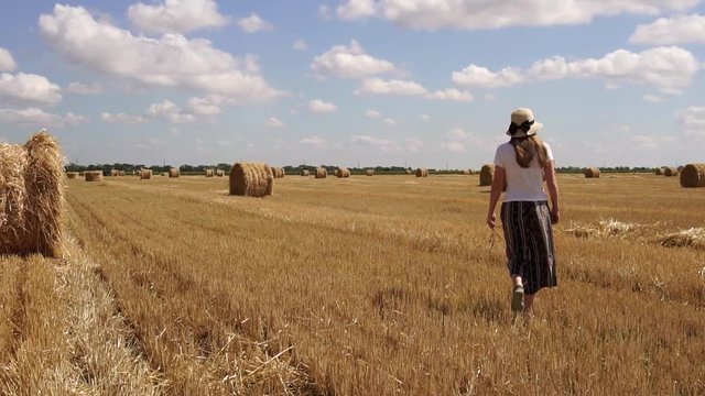 Young woman in casual clothes having a relaxing walk around hot sunny wheat field on summer countryside in slow motion