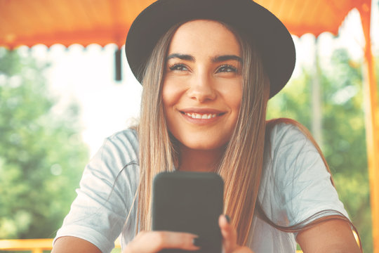 Young hipster girl in trendy hat holding smartphone in hands smi
