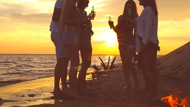 Friends clinking beer bottles on the beach during the sunset.