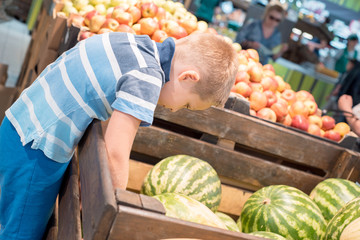 Boy sits in the shopping trolley with watermelon and other products bought by parents