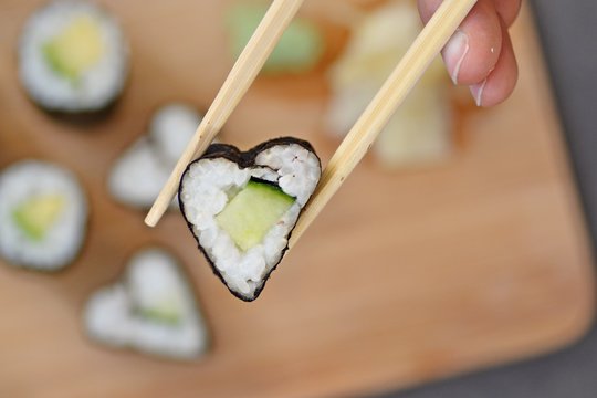 Eat heart shaped sushi with cucumber with chopsticks - close up as a symbol of being in love with sushi