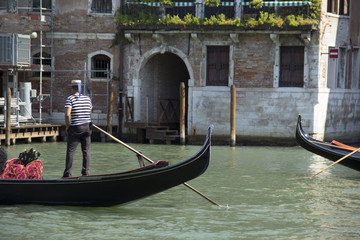 Fototapeta na wymiar Venice - August 27: Gondolier drives a gondola with tourists on board on the Grand Canal on August 27, 2018 in Venice, Italy