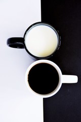 Two cups in front of a half black and half white background, one cup contains coffee, the other milk and both creat a contrast, concept for yin and yang with coffee cups