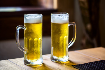 Two glasses with cold beer on wooden table in restaurant.