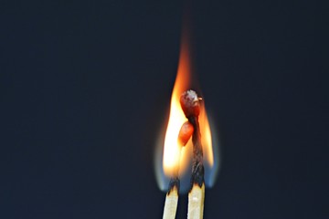 Two burning matches against a black background look like a couple cuddling and being intimate with...