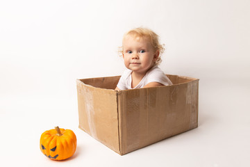 caucasian little girl baby sitting in corton box on white background and afraid of pumpkin jack-lantern halloween