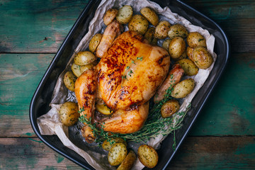 Roasted chicken with thyme served on black baking dish with potatoes, oranges and spices on wooden table. Thanksgiving or Christmas dinner. Top view