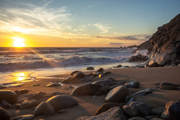 une plage au coucher de soleil avec du sable et des grosses pierres en premier plan