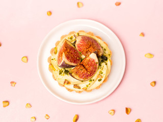 Delicious tart with fresh figs and pistachios on pink pastel backgrounds, top view