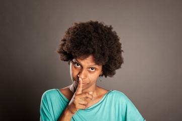 Obraz na płótnie Canvas portrait of black woman showing silence gesture on a gray background