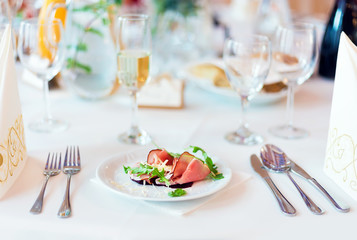 Prosciutto with parmesan cheese and rucola as a starter for wedding dish on the white table settings, light blurred background