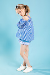 A girl in a T-shirt and shorts with glasses on her head is standing on a blue background.