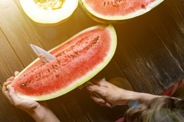 teenager slicing fresh watermelon with knife on a wooden table on summer day f